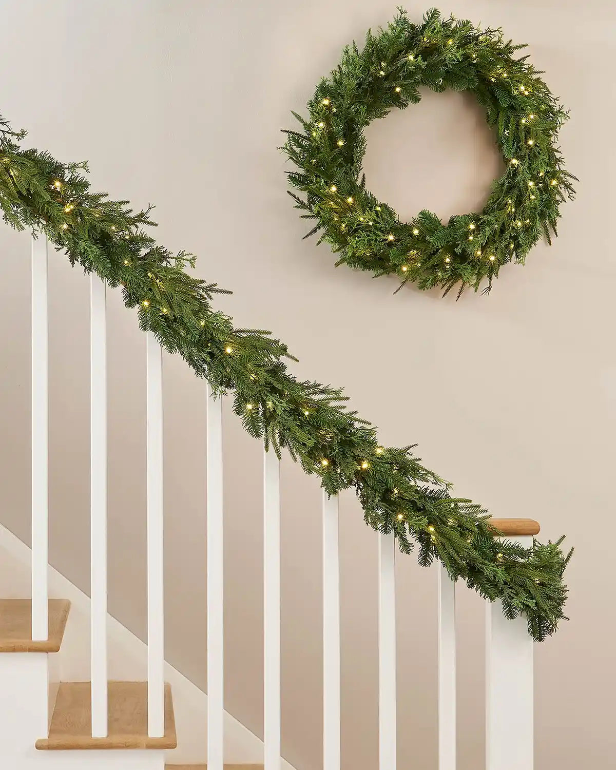 Green garland draped around white wooden staircase banister with matching green circle garland hanging on the wall above