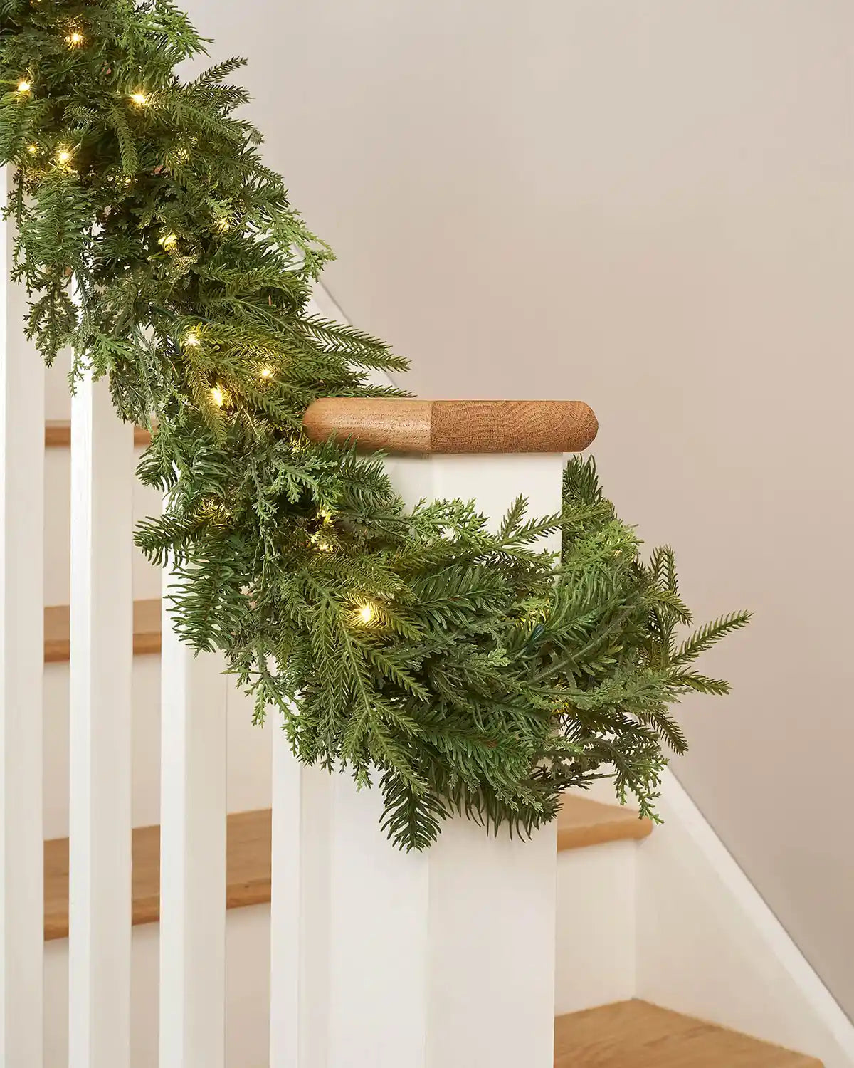 Green garland with interwoven warm white lighting wrapped around a wooden staircase banister 