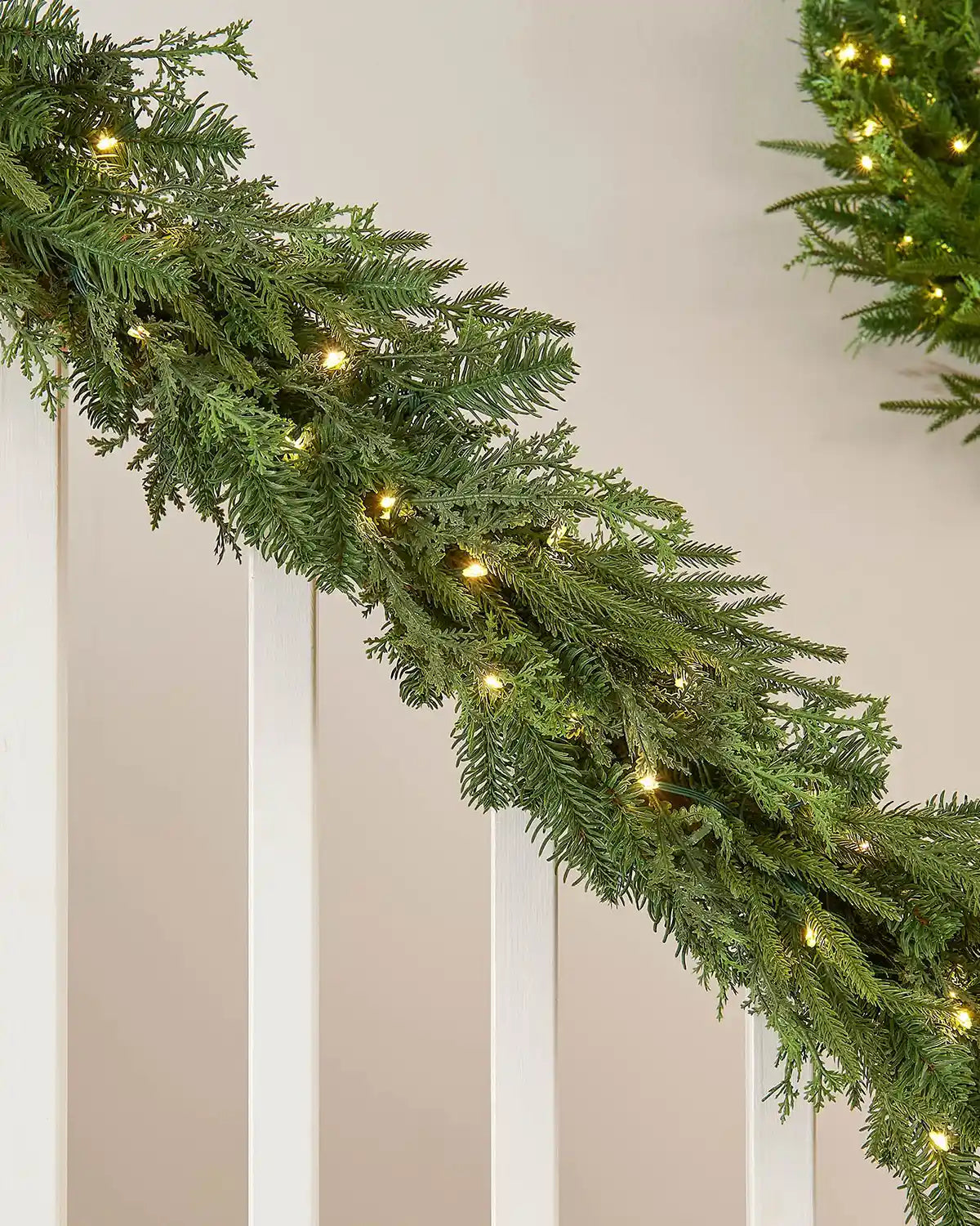 Green garland with interwoven warm white lighting draped around a white staircase banister