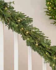 Green garland with interwoven warm white lighting draped around a white staircase banister