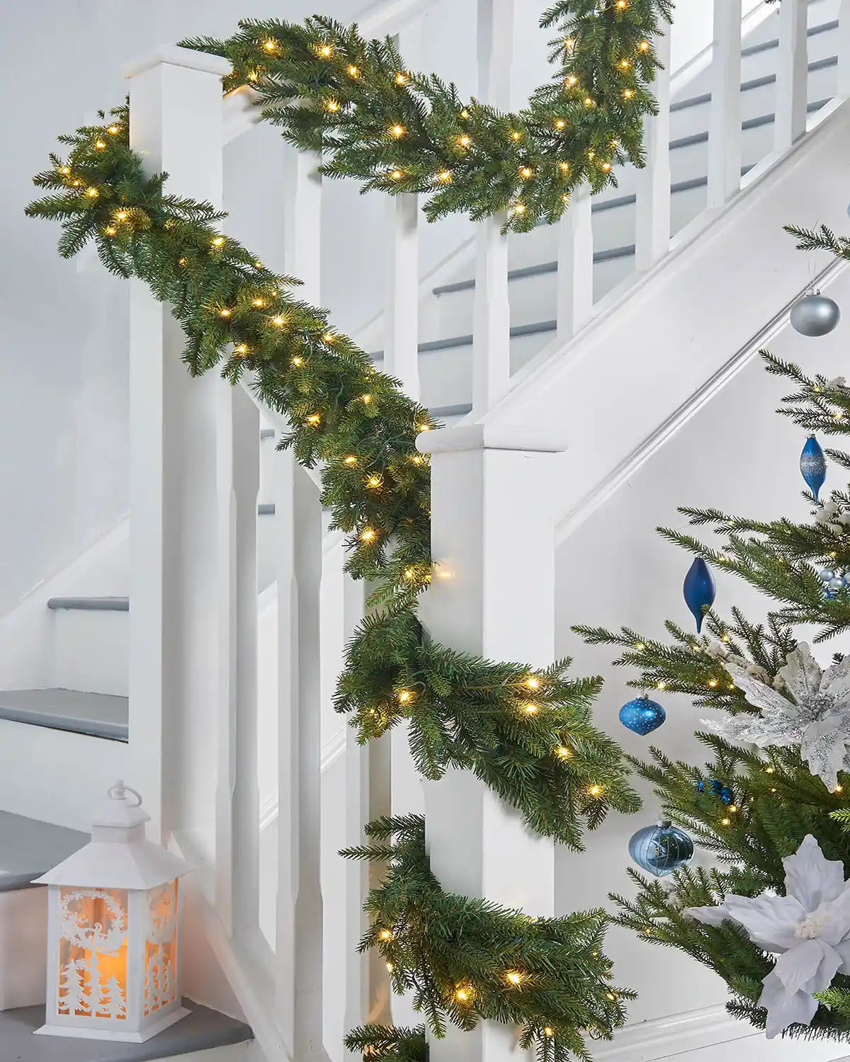 Green garland wrapped around a white staircase banister on against a white wall