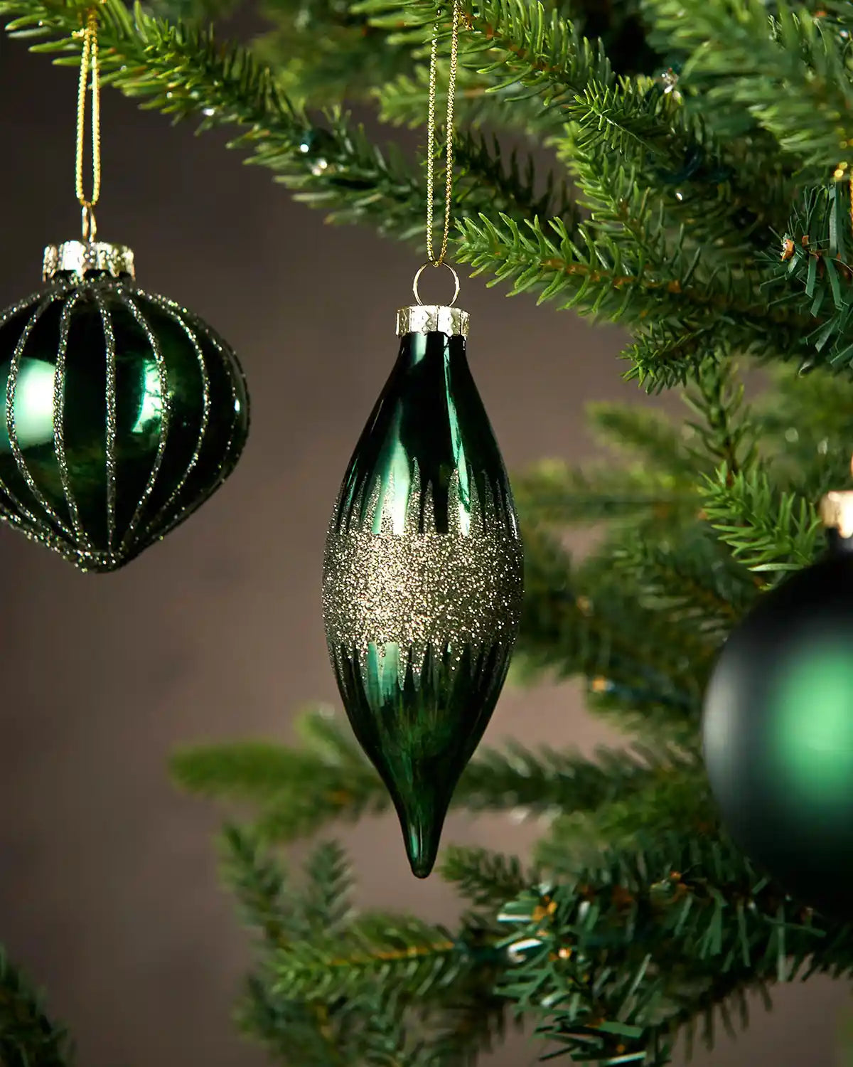 Green glass bauble on a Christmas tree with a neutral background