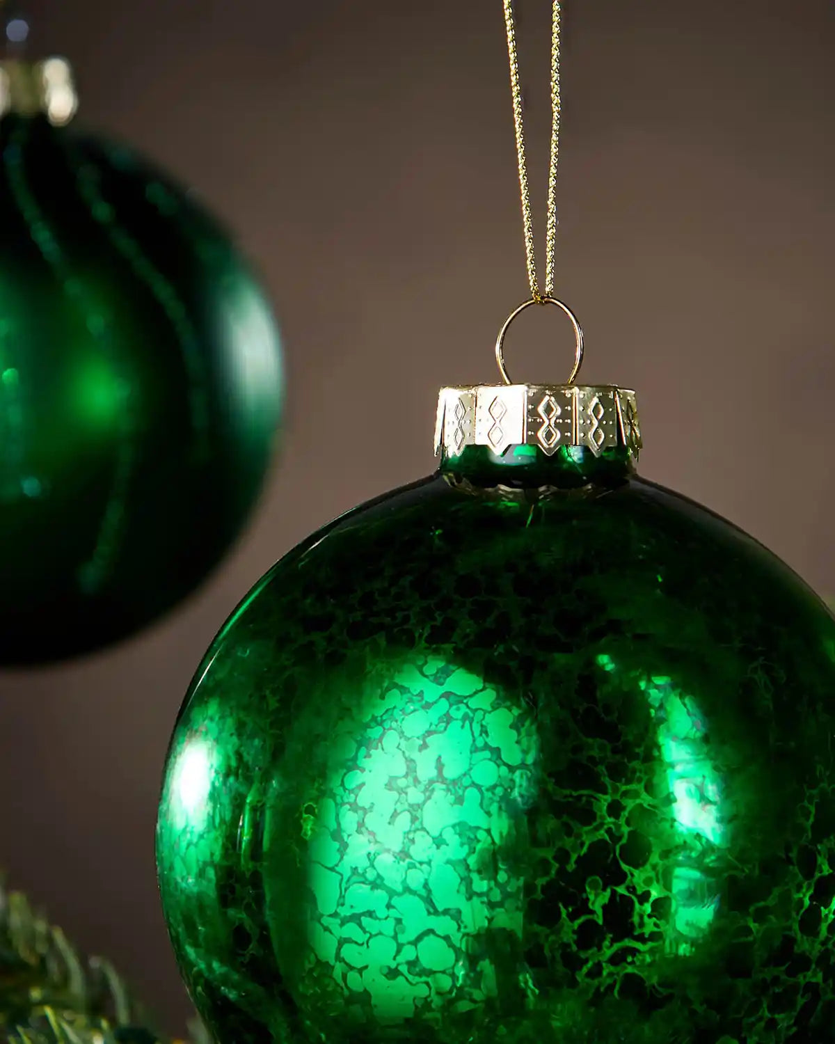 Green glass ornament with textured surface and gold cap on a plain background