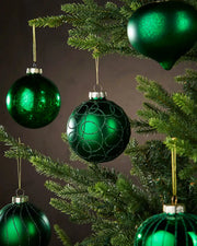 Green glass ornaments hanging on a Christmas tree against a dark background