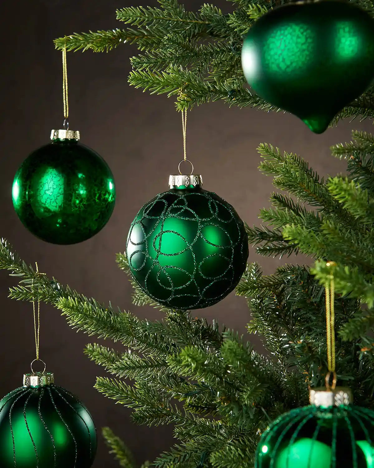 Green glass ornaments hanging on a Christmas tree against a dark background
