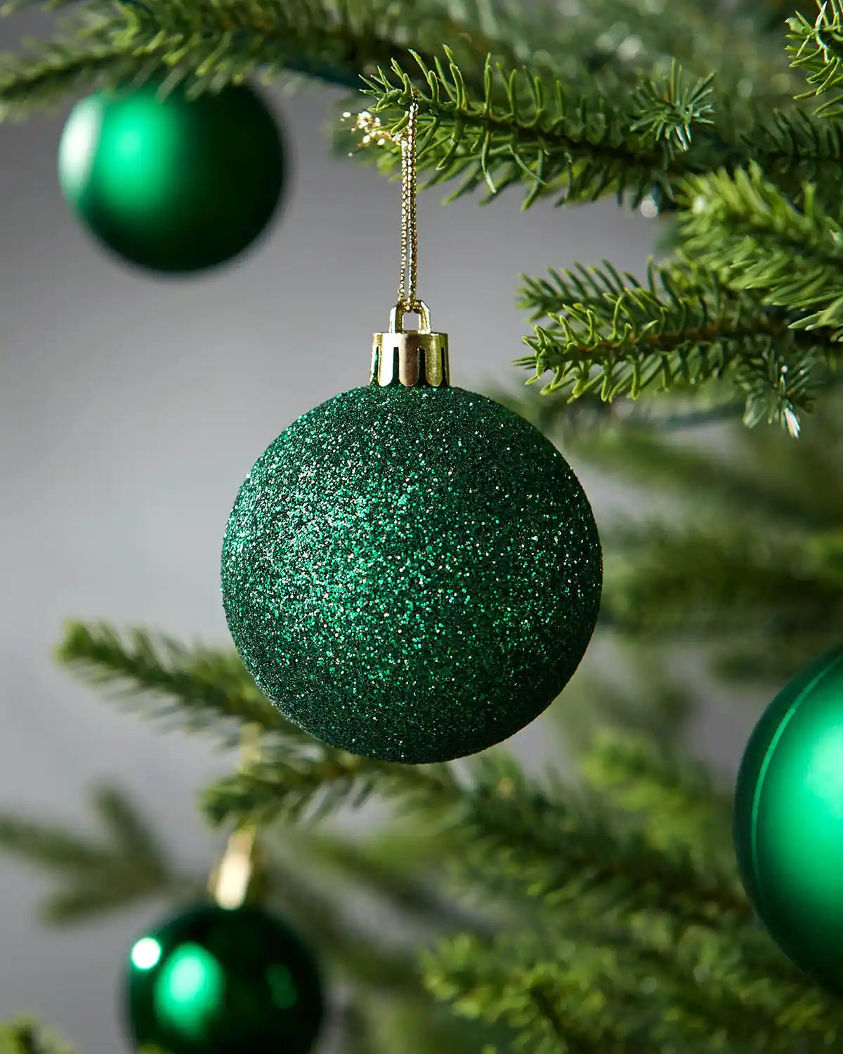 Green glittery Christmas baubles on a tree with a blurred background