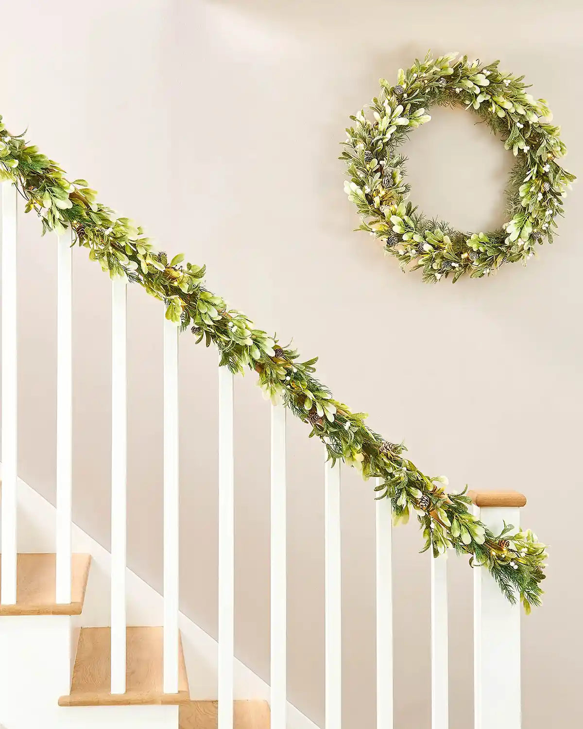 Green leafy garland and wreath on a staircase railing against a Beige wall.