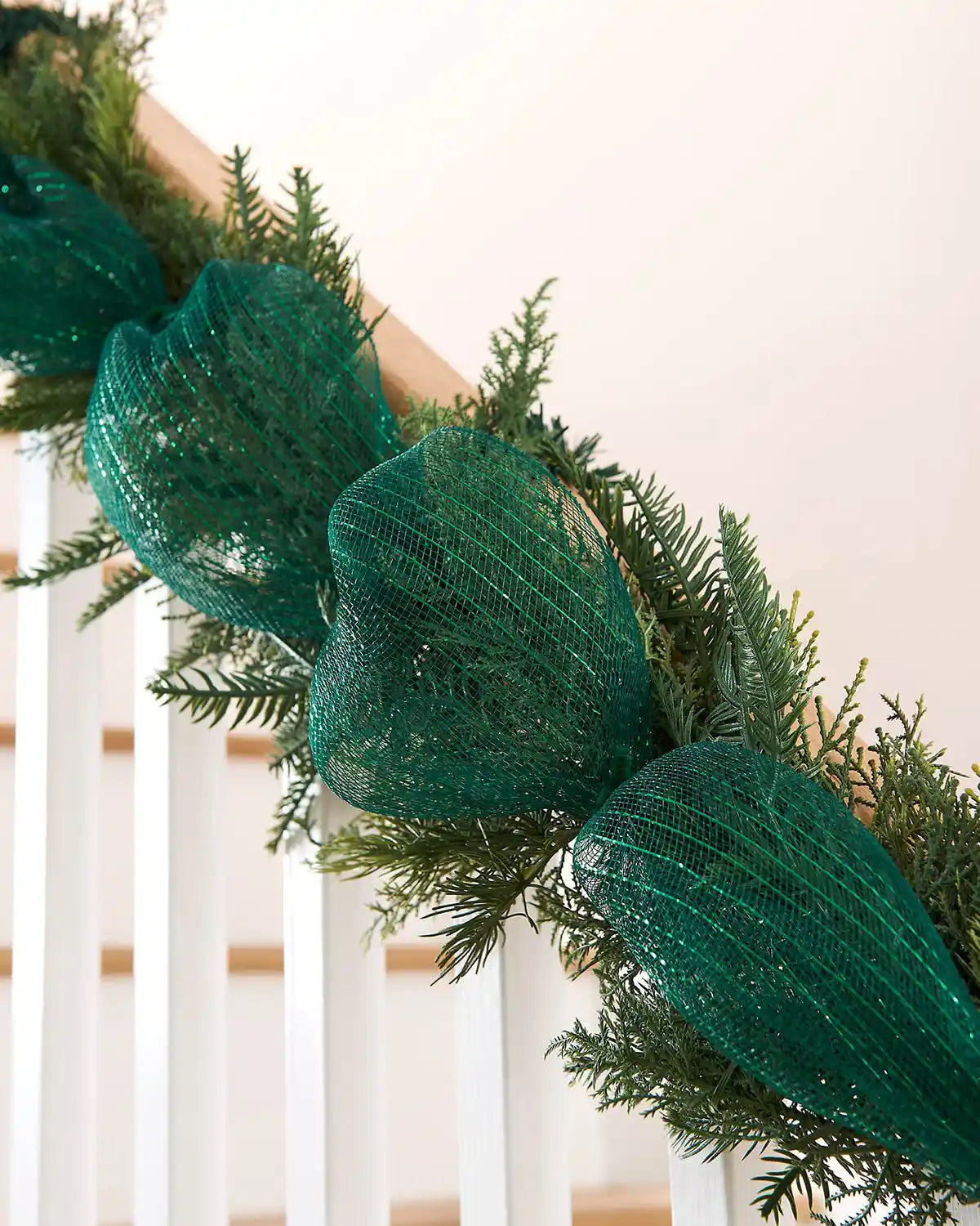 Green mesh ribbon wrapped around a garland on a staircase banister against a cream wall
