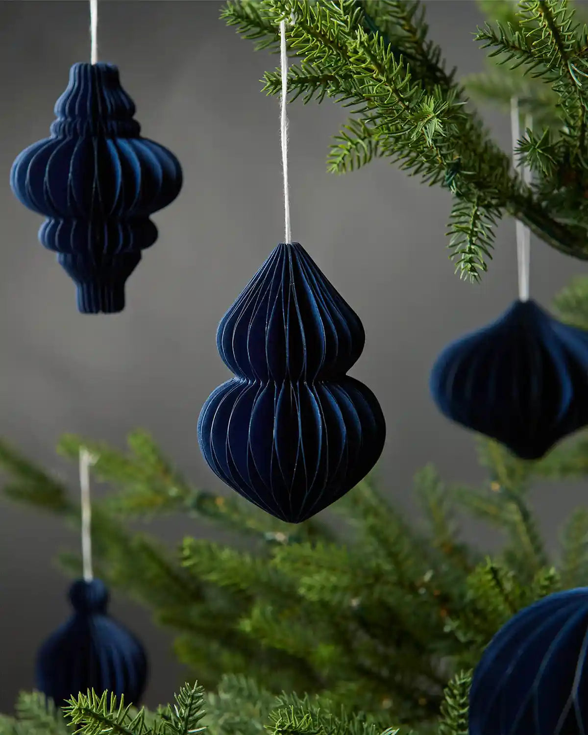 A group of 10cm navy blue honeycomb paper hanging Christmas tree decorations on tree in front of grey wall background