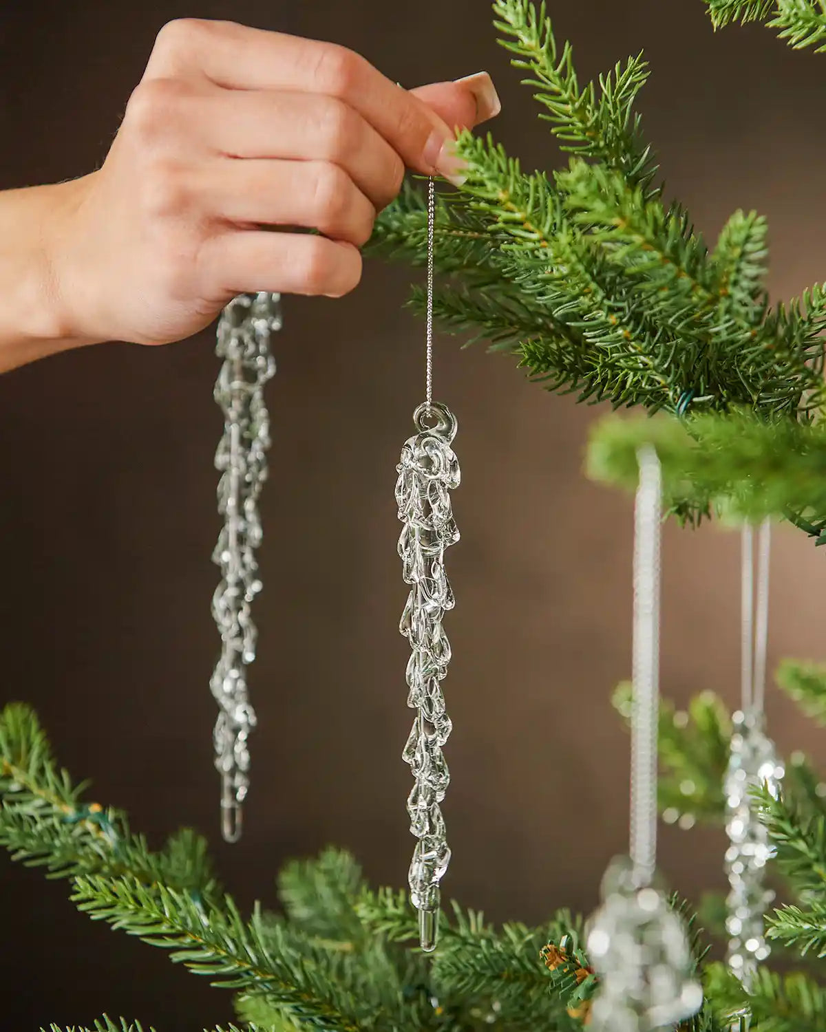 Hand holding a crystal ornament on a Christmas tree branch with a blurred brown background