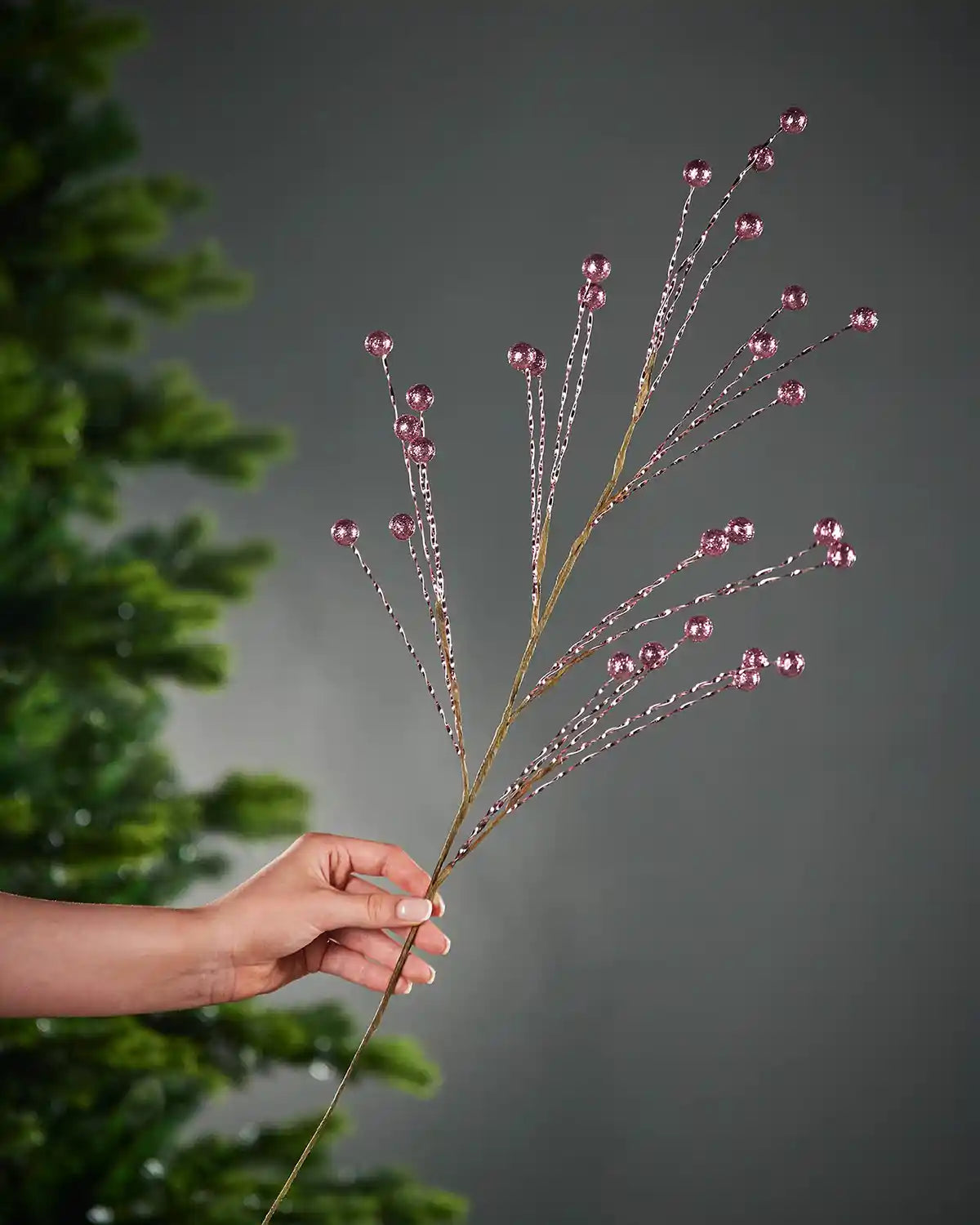 Hand holding a decorative Pink vine with pink beads against a grey background