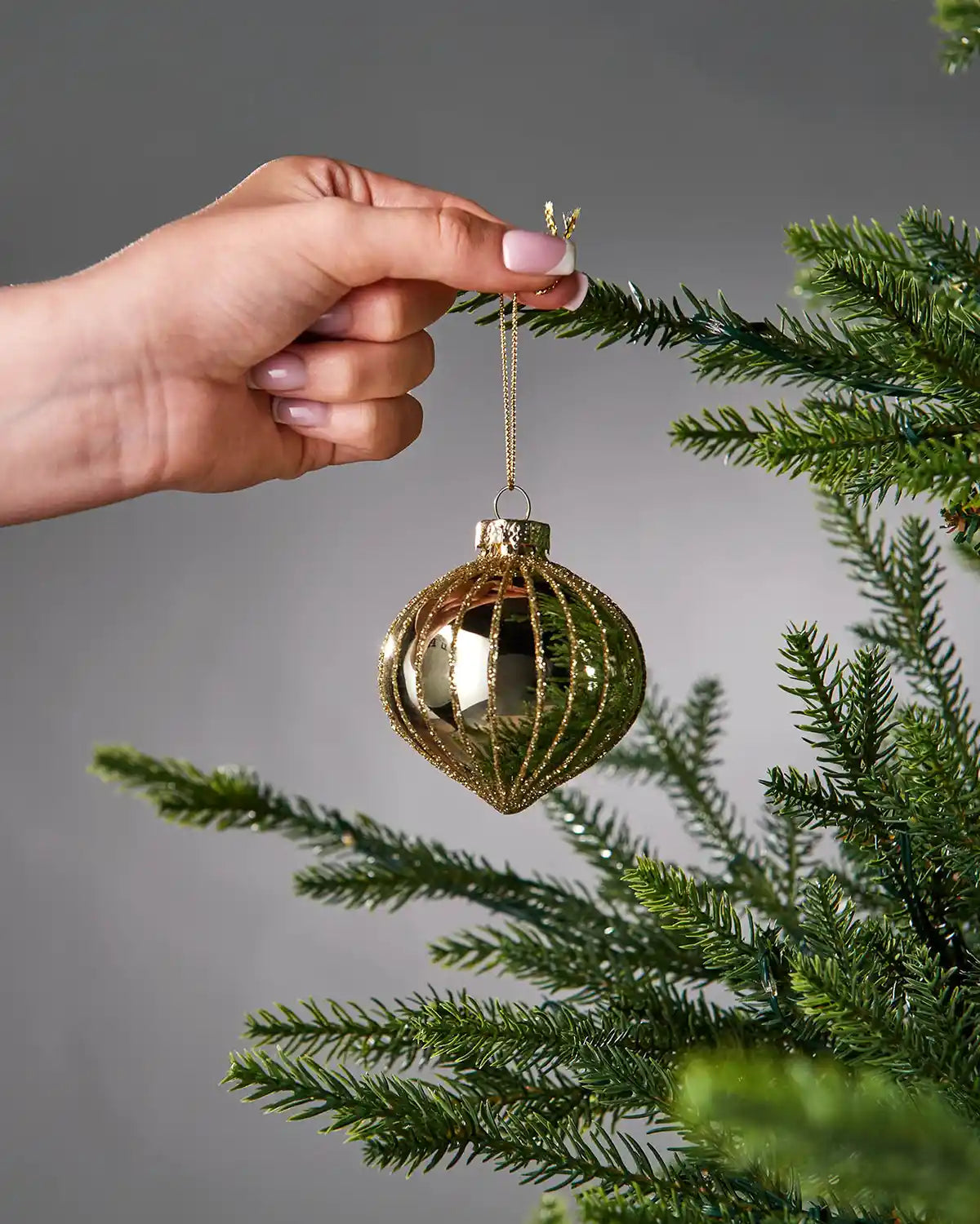 Hand holding a gold Christmas bauble on a tree branch with a grey background