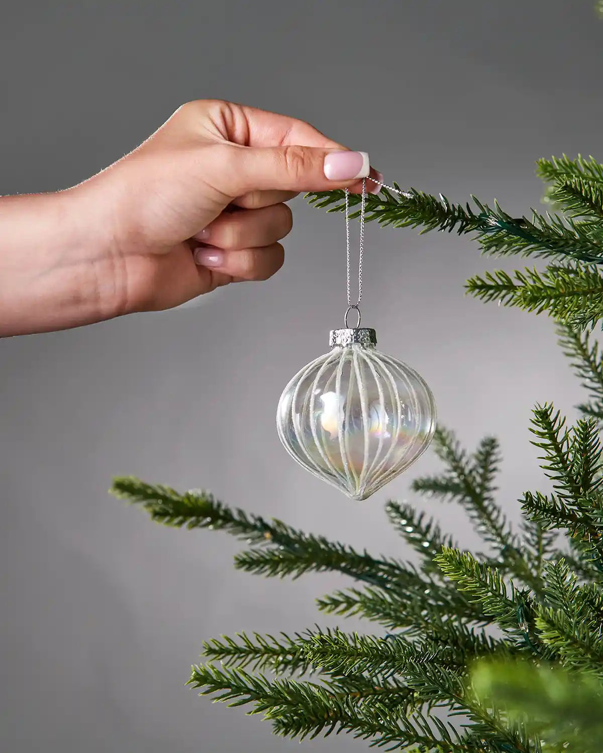 Hand holding a iridescent glass bauble with ribbed design against a grey background