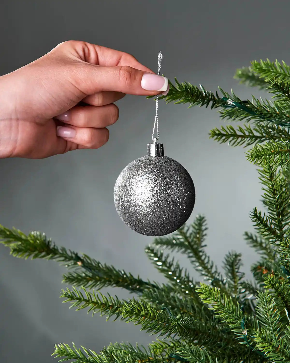 Hand holding a silver glittery Christmas bauble against a tree branch.
