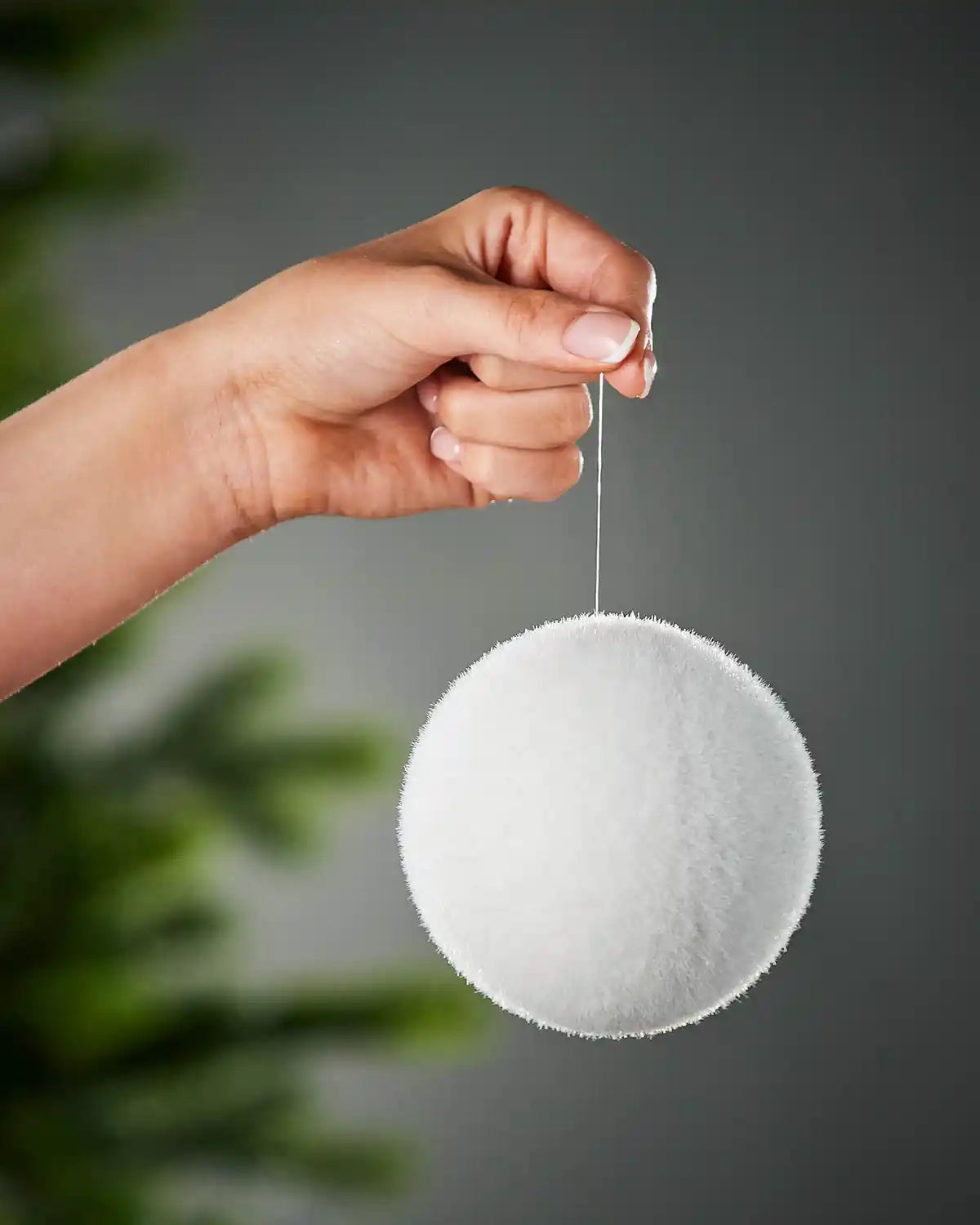 Hand holding a white snowball bauble ornament against a grey background