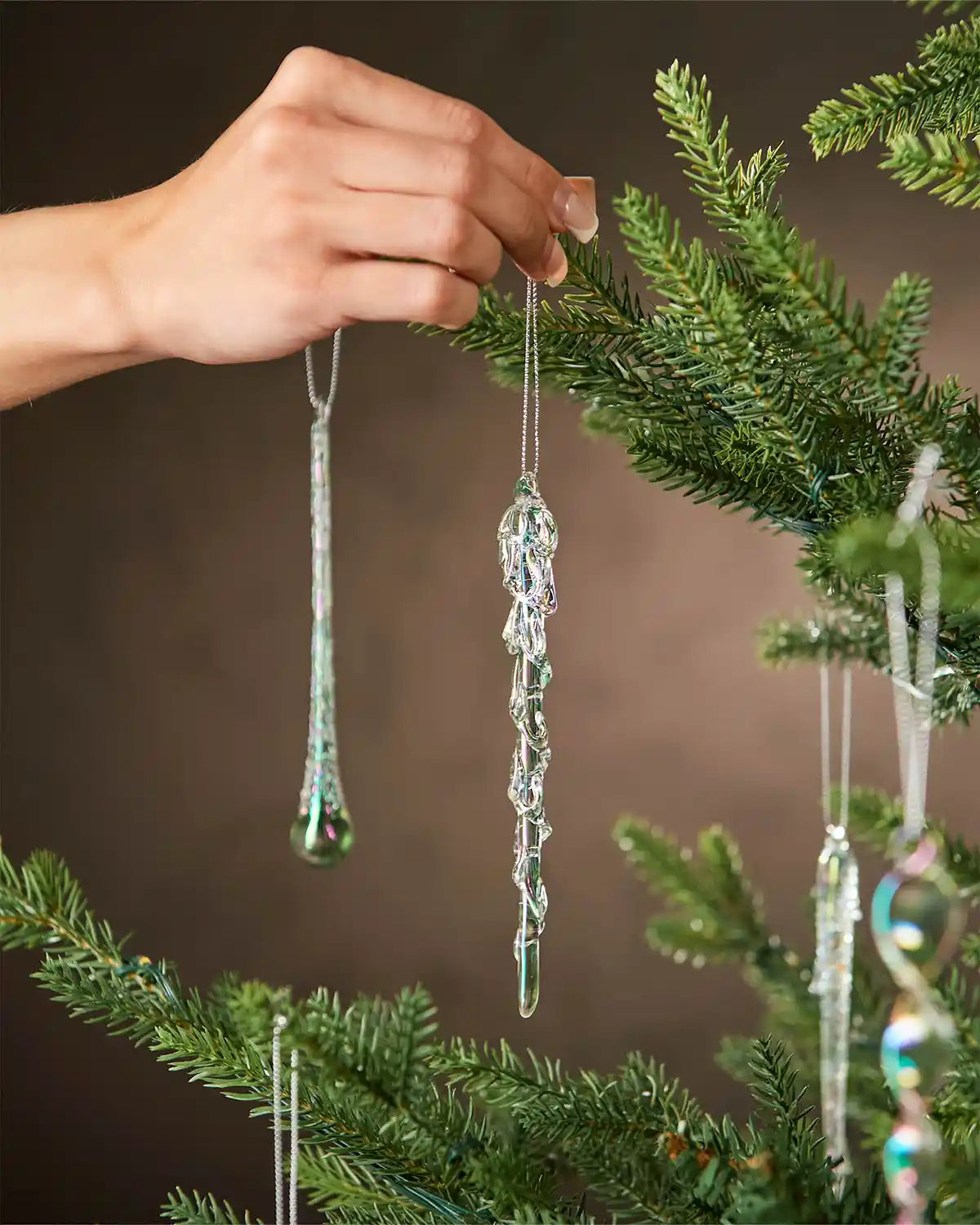 Hand placing a decorative ornament on a Christmas tree with a blurred background