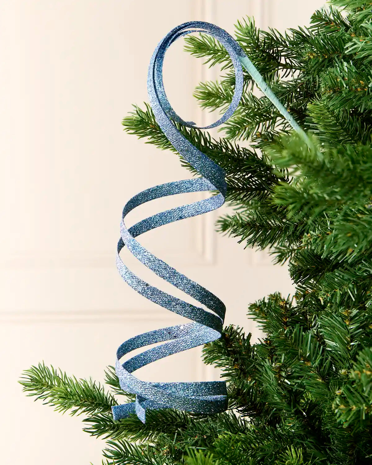 Ice Blue Glitter Spiral Swirl Pick hanging from Christmas tree branch with cream background