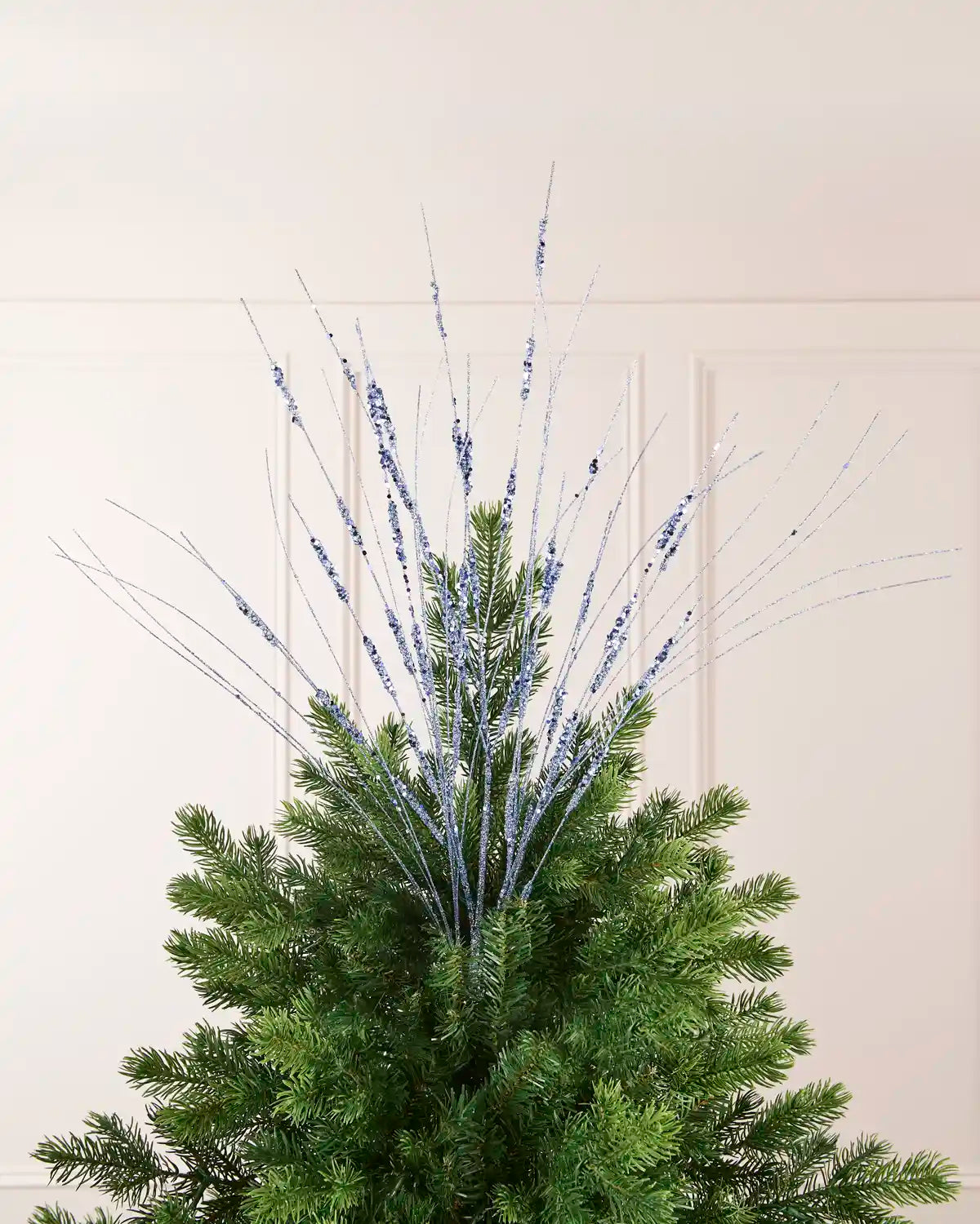 Ice Blue Glitter Wispy Spray displayed at the top of a Christmas tree, with thin glitter-covered stems extending upward and outward
