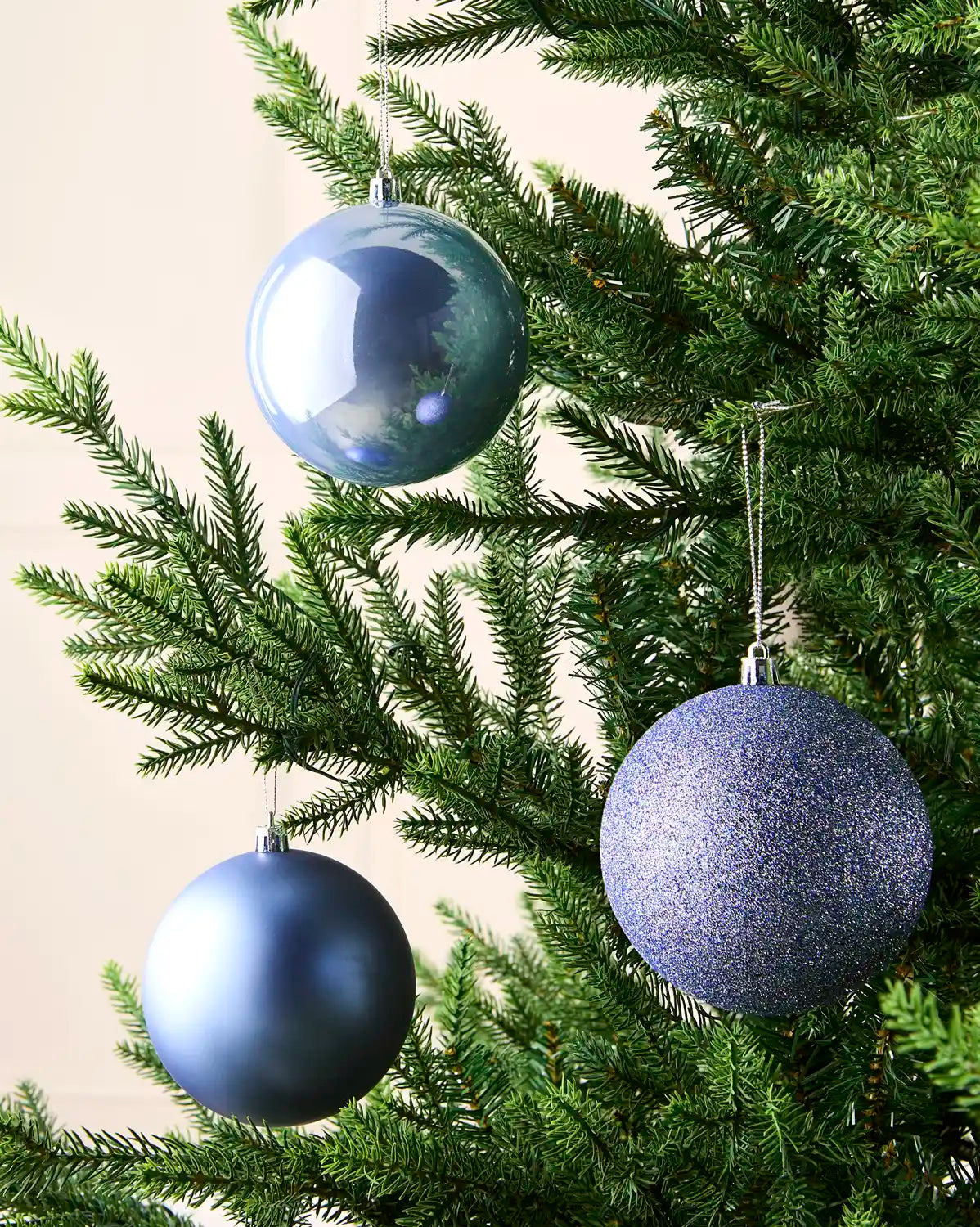 Ice Blue baubles hanging on a Christmas tree against a cream wall