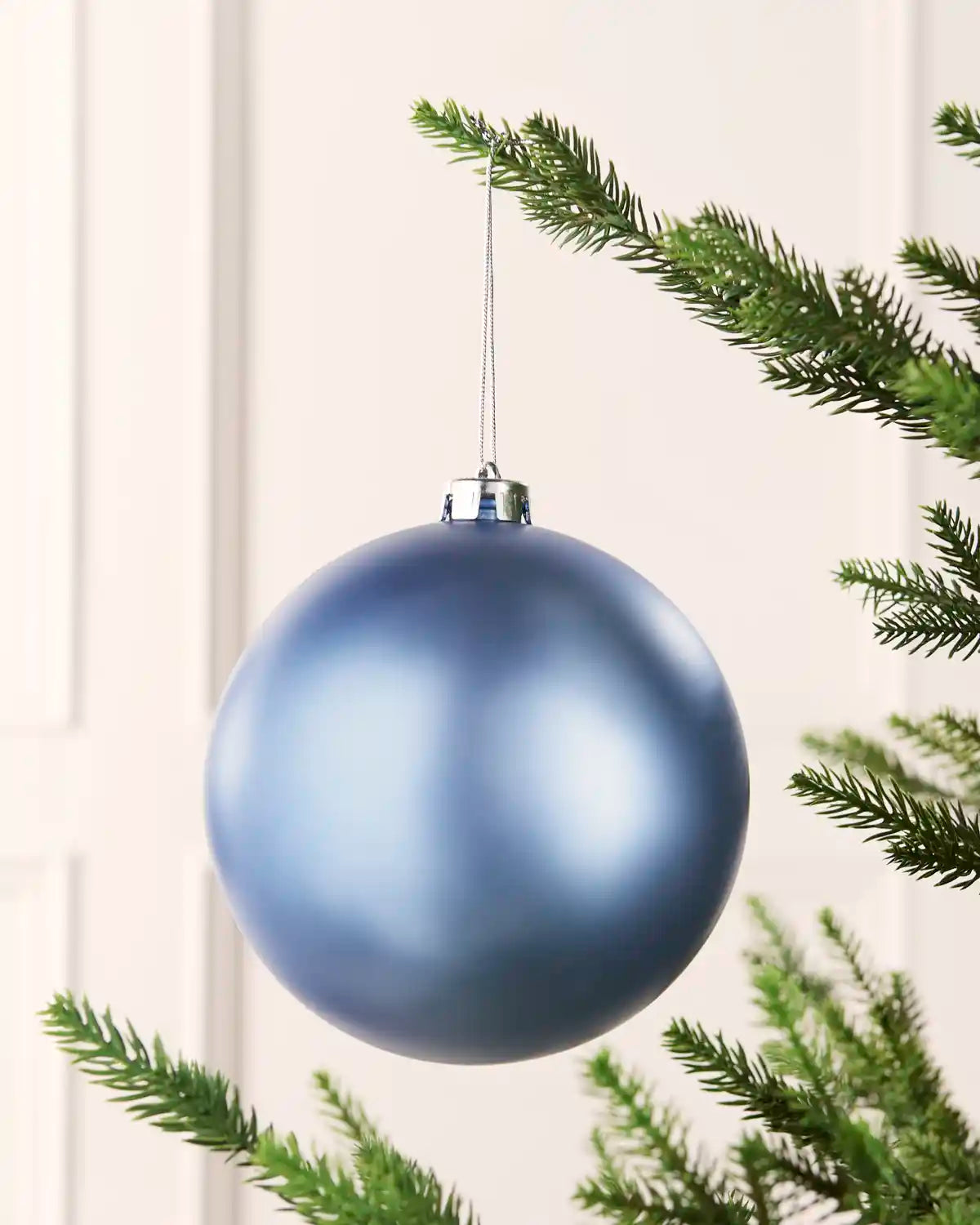 Ice blue 15 cm oversized Matt shatterproof bauble hanging on a Christmas tree with a silver cap and matching string.
