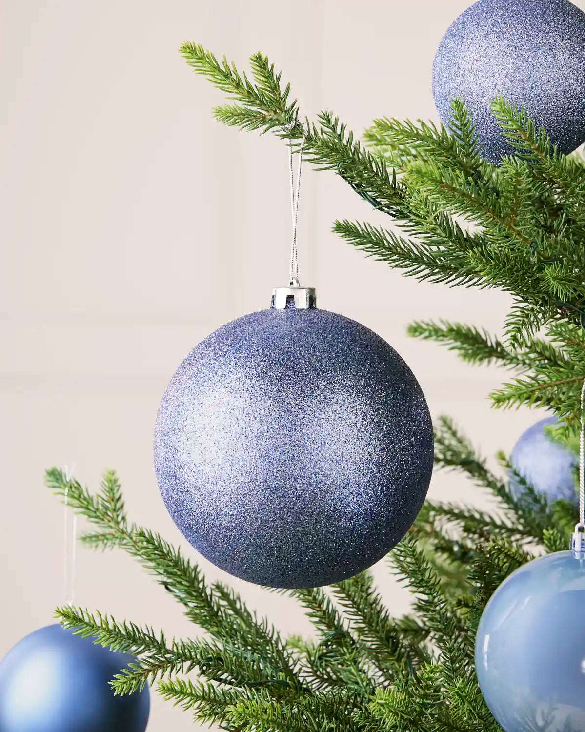 Ice blue 15 cm oversized glitter shatterproof bauble displayed on a Christmas tree with coordinating ice blue baubles.
