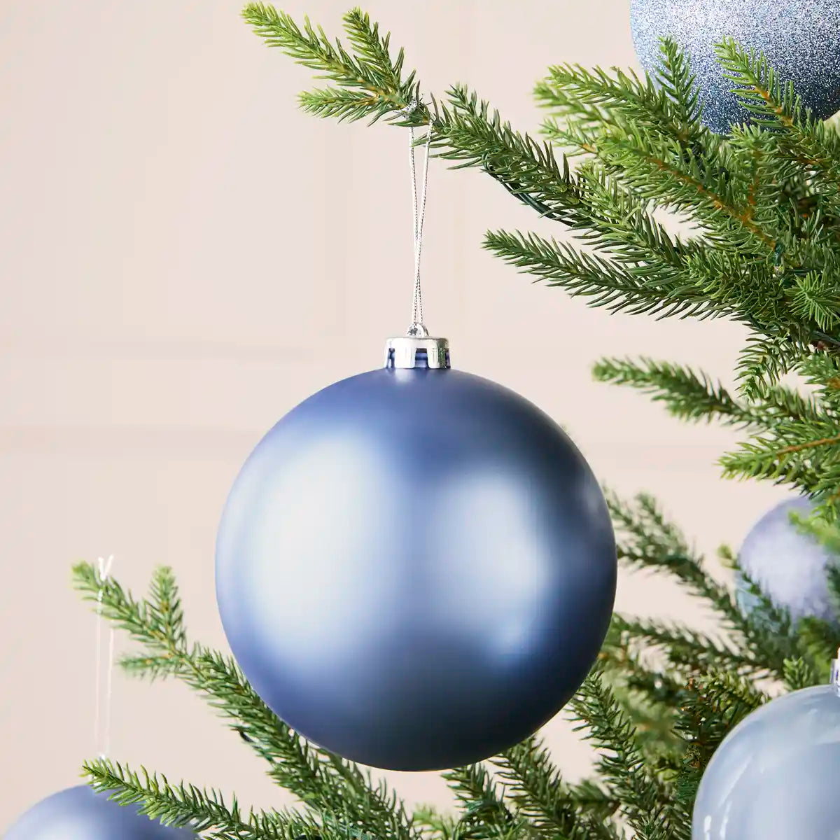 Ice blue 15 cm oversized matt shatterproof bauble displayed on a Christmas tree with coordinating ice blue baubles.
