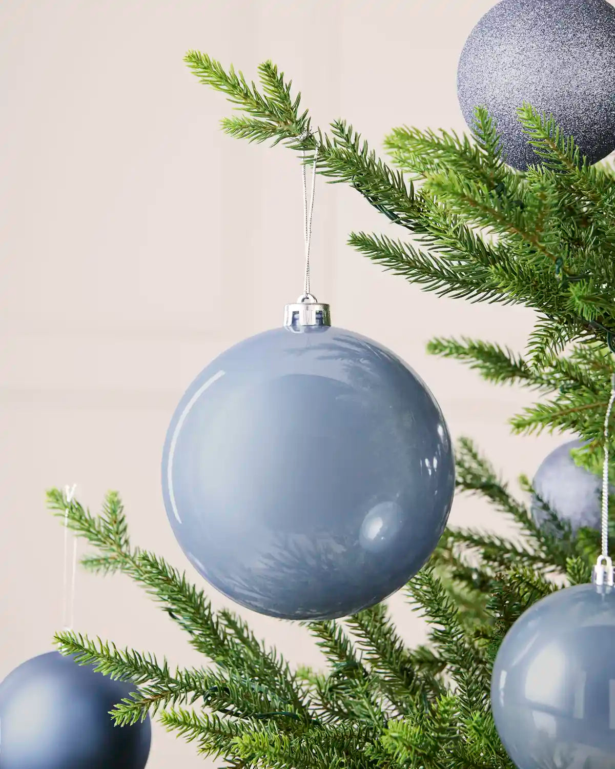 Ice blue 15 cm oversized shiny shatterproof bauble displayed on a Christmas tree with coordinating ice blue baubles.
