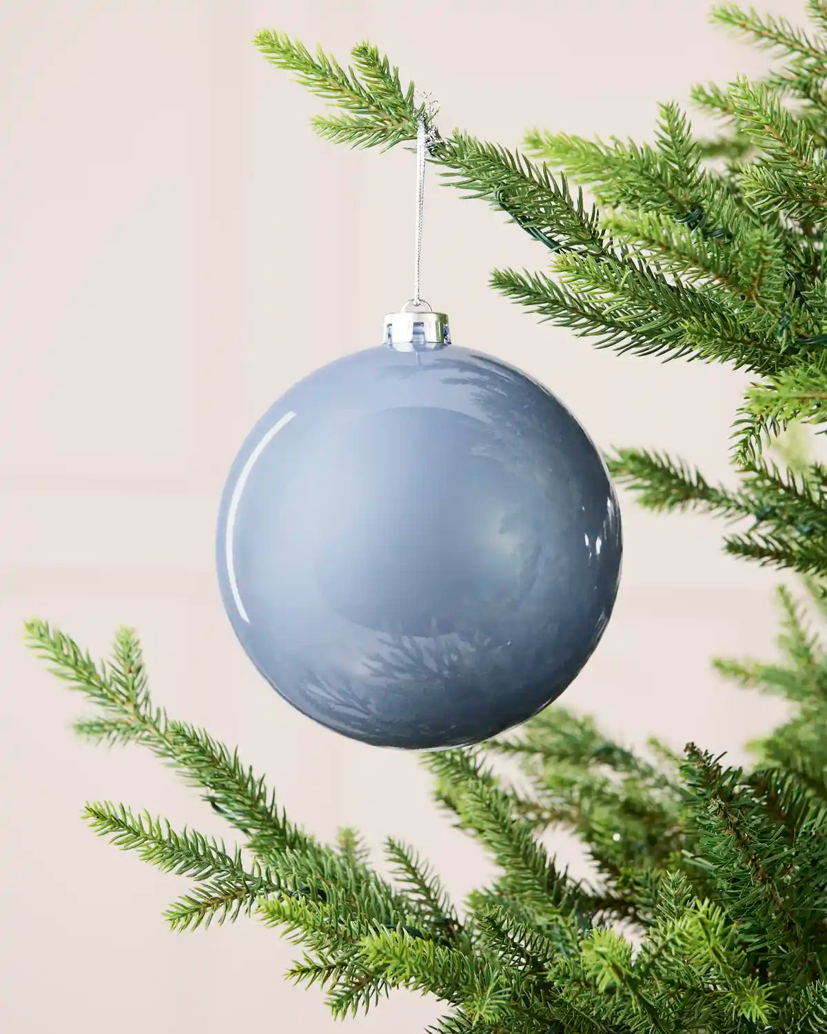 Ice blue 15 cm oversized shiny shatterproof bauble hanging on a Christmas tree with a silver cap and matching string.