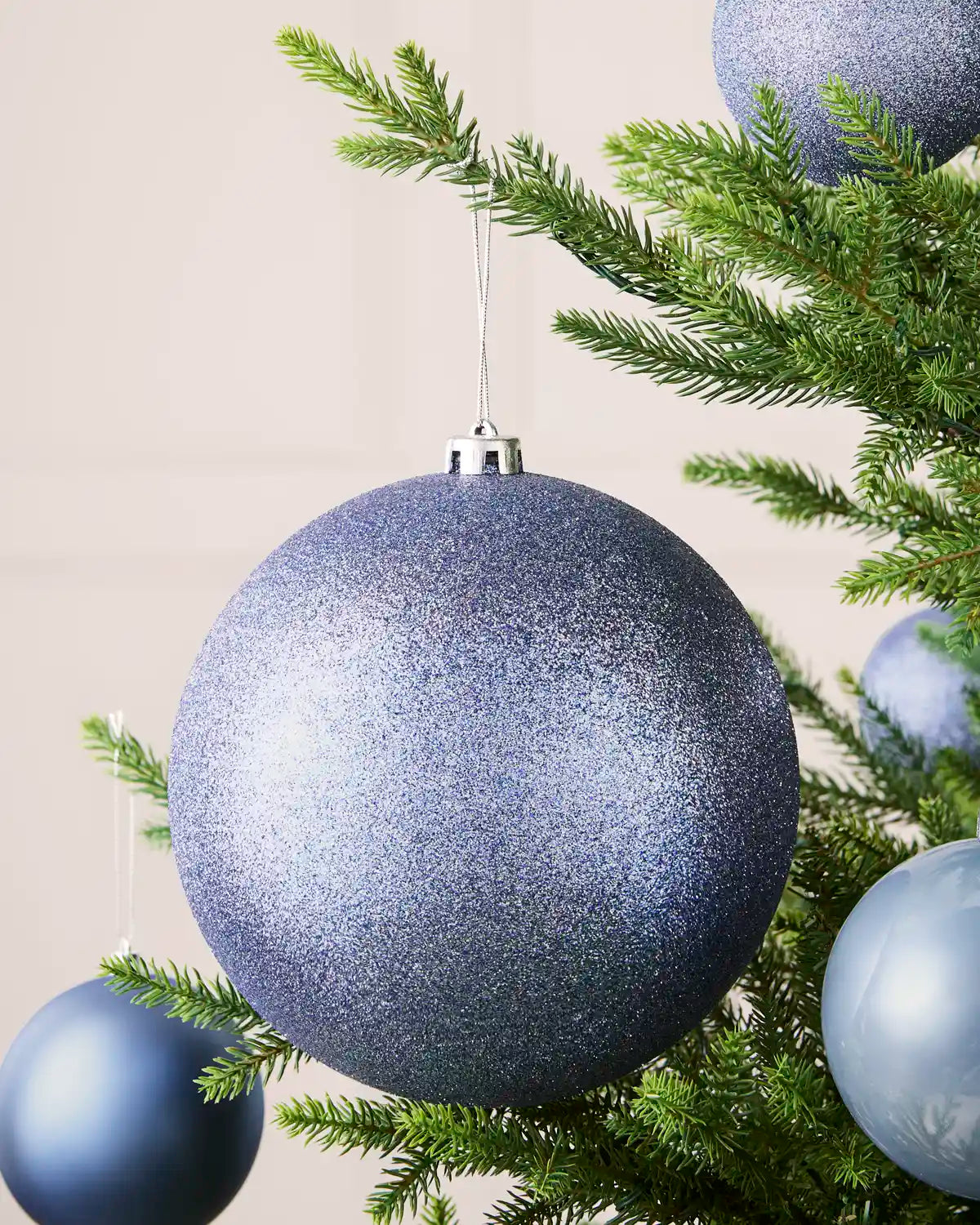 Ice blue 20 cm oversized glitter shatterproof bauble displayed on a Christmas tree with coordinating ice blue baubles.
