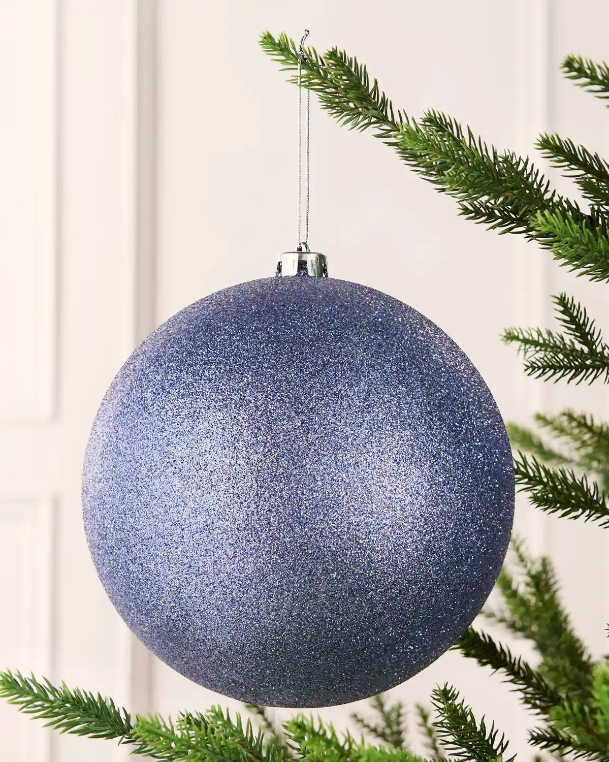 Ice blue 20 cm oversized glitter shatterproof bauble hanging on a Christmas tree with a silver cap and matching string.
