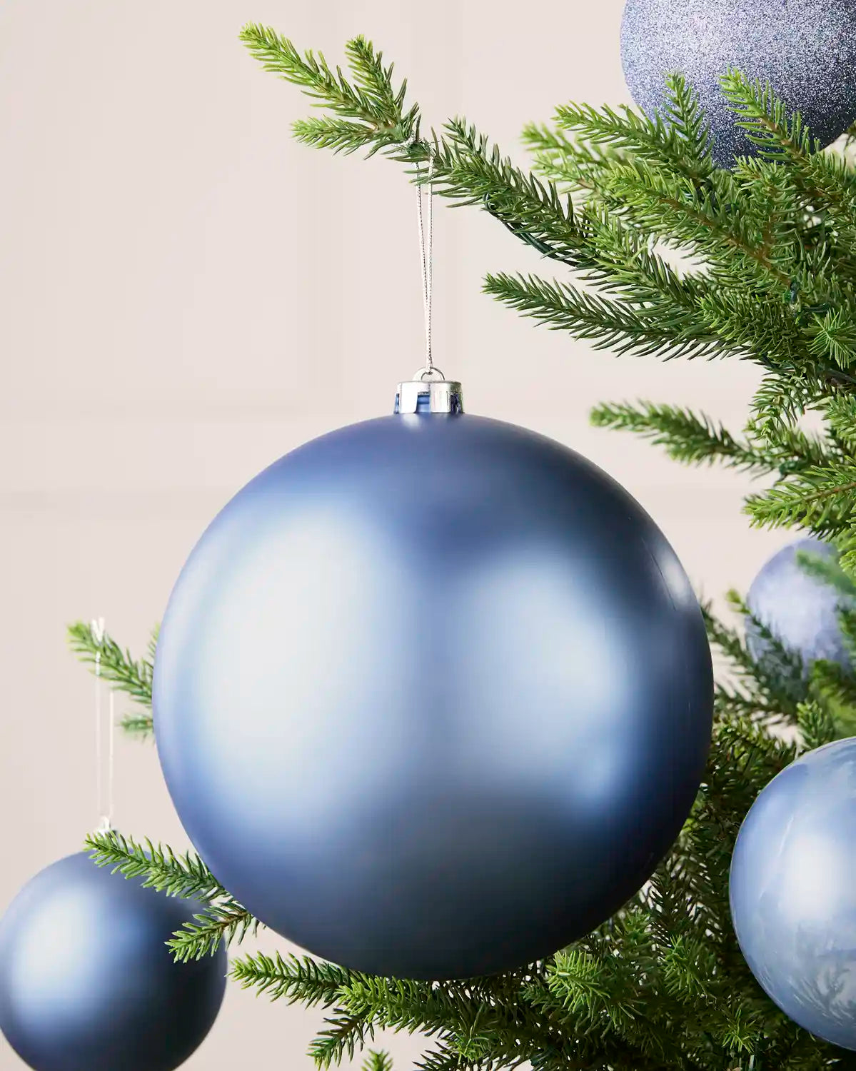 Ice blue 20 cm oversized matt shatterproof bauble displayed on a Christmas tree with coordinating ice blue baubles.
