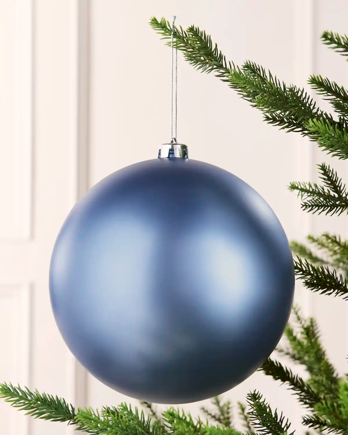 Ice blue 20 cm oversized matt shatterproof bauble hanging on a Christmas tree with a silver cap and matching string.
