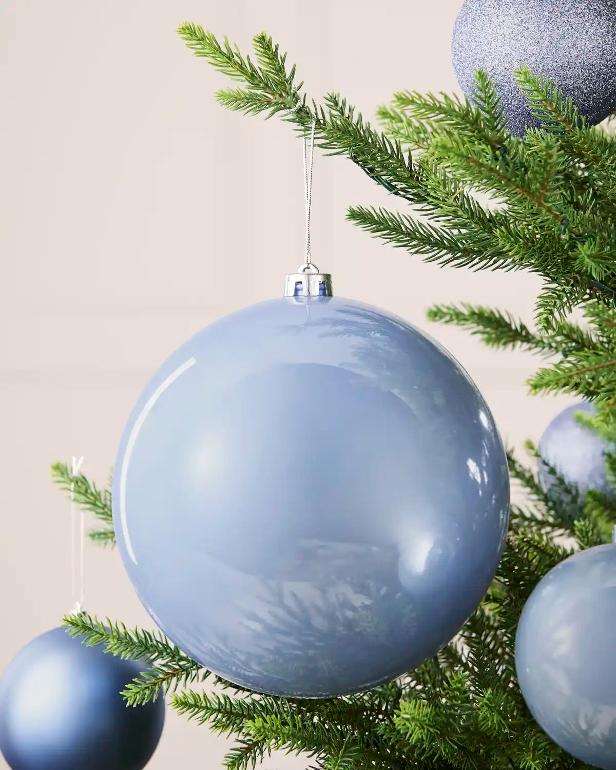 Ice blue 20 cm oversized shiny shatterproof bauble displayed on a Christmas tree with coordinating ice blue baubles.
