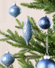 Ice blue glass baubles hanging from Christmas tree branches in teardrop, onion and classic round shapes with a blurry cream background.