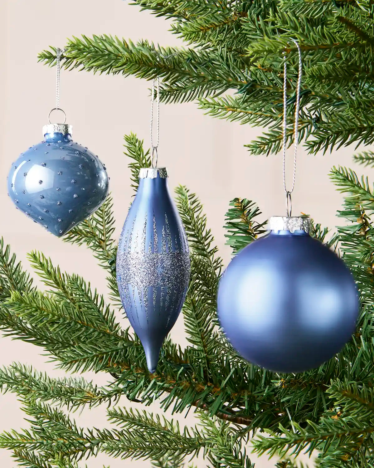 Ice blue glass baubles hanging from Christmas tree branches in teardrop, onion and classic round shapes with glitter detailing
