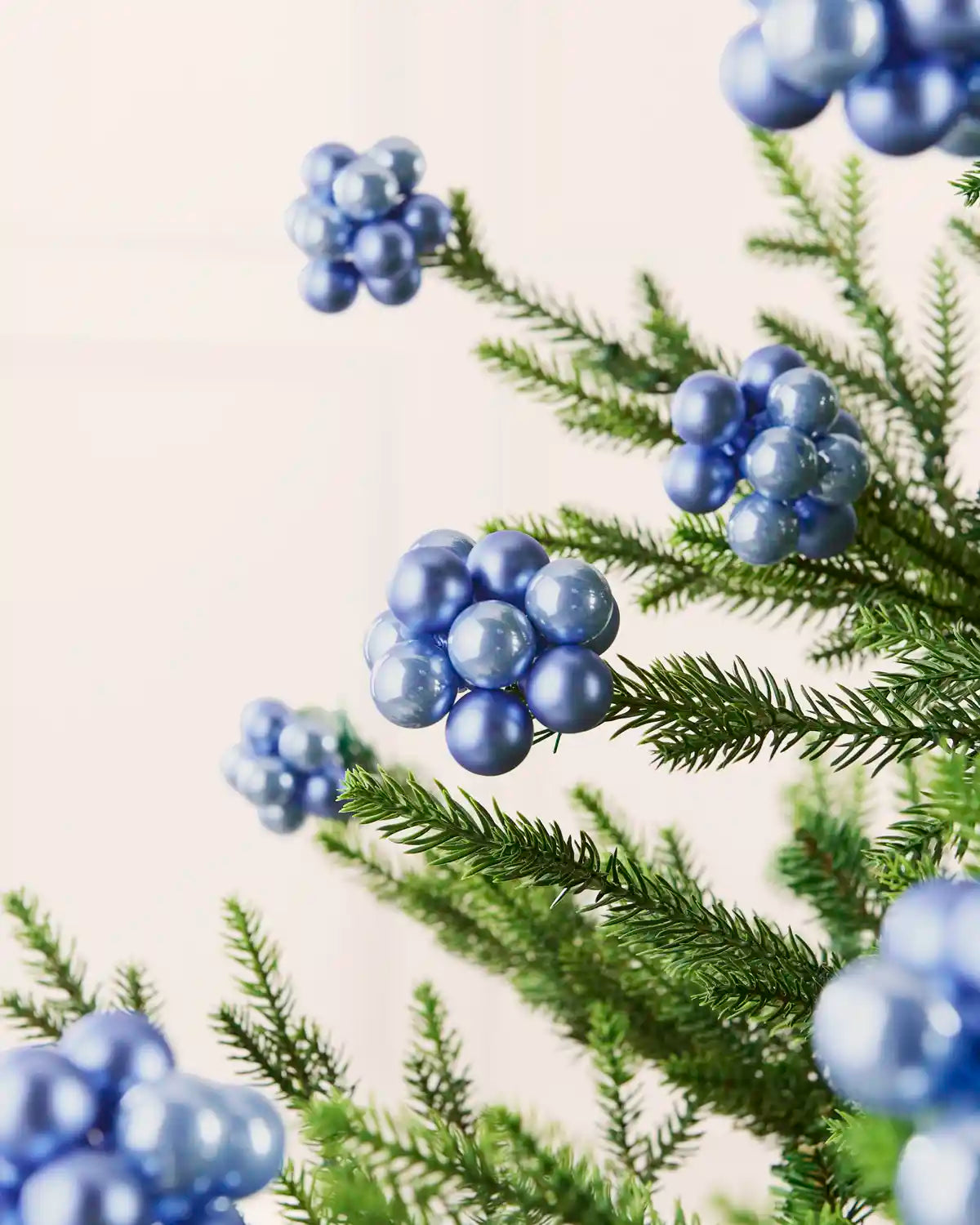 Ice blue glass berry cluster baubles arranged throughout a green Christmas tree.

