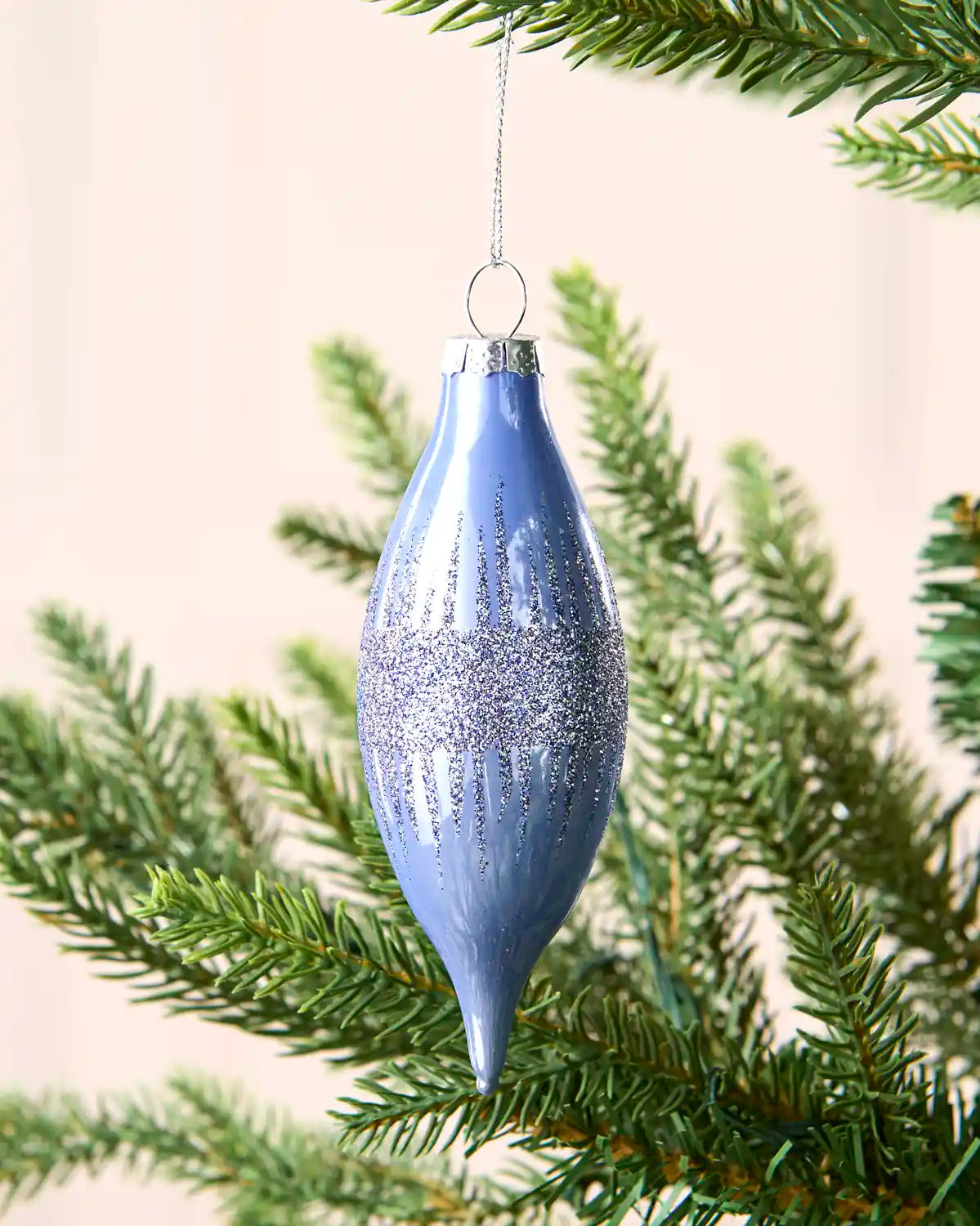 Ice blue hanging bauble on a Christmas tree branch against a cream wall 