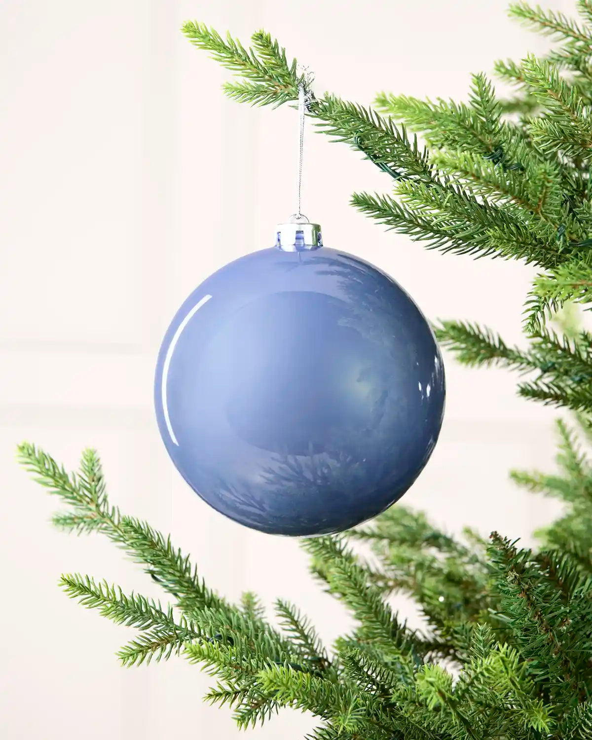 Ice blue shiny oversized bauble hanging on a Christmas tree against a cream background