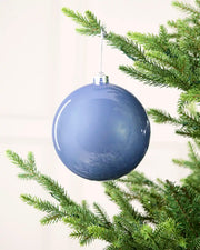 Ice blue shiny oversized bauble hanging on a Christmas tree against a cream background