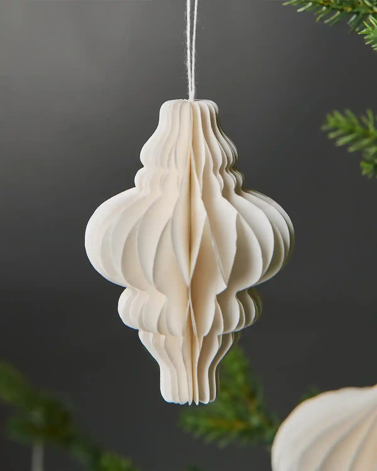 Close-up of individual 10cm off-white paper decoration hanging from Christmas tree in front of grey background