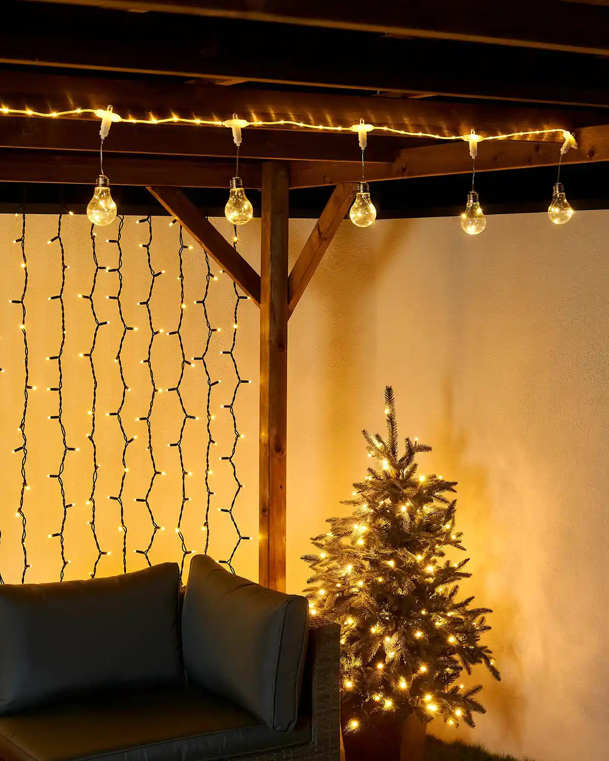 Indoor setting with string lights hanging from a wooden beam, a small tree with lights, and a sofa.