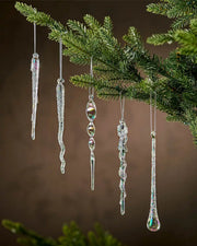 Iridescent icicle ornaments hanging on a Christmas tree branch against a brown background