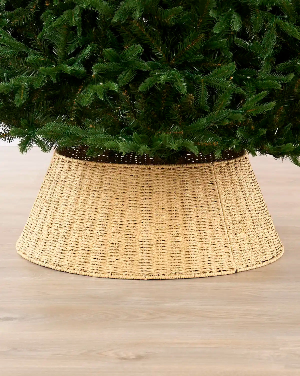 Knitted Rattan Christmas Tree Collar shown around a Christmas tree in a natural woven finish