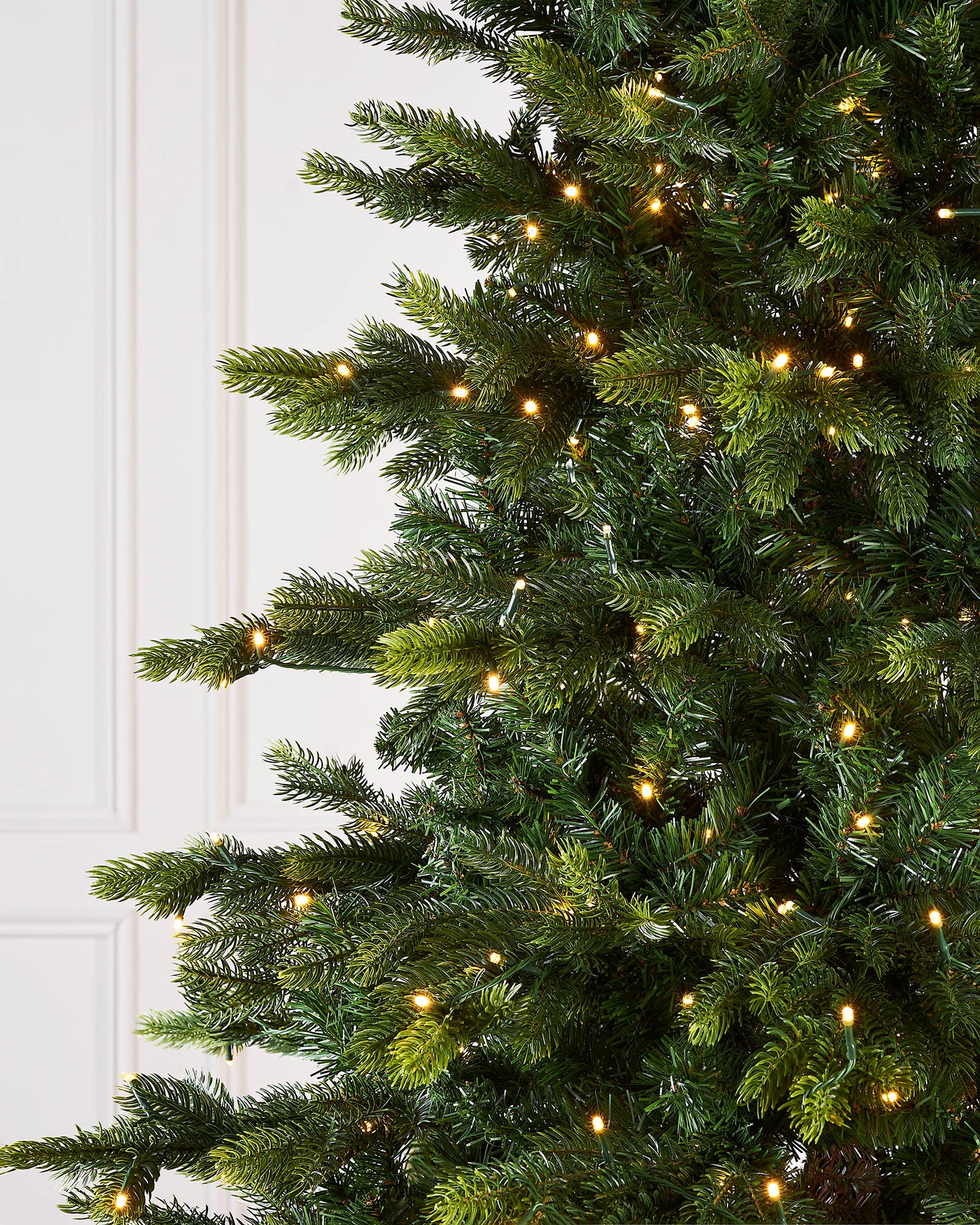 Close-up of a Christmas tree with lights against a white door.