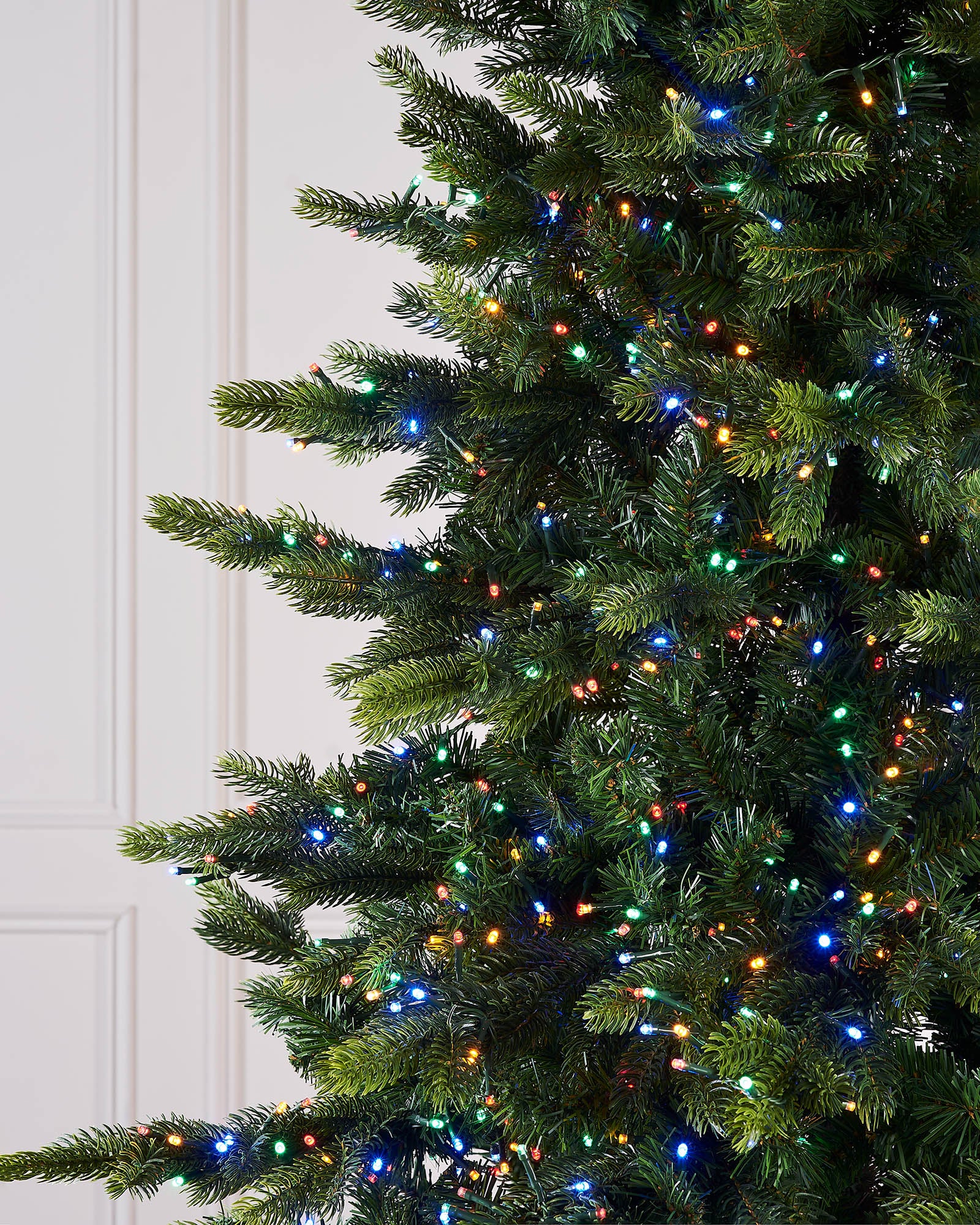 Close-up of a Christmas tree with colorful lights against a white door.