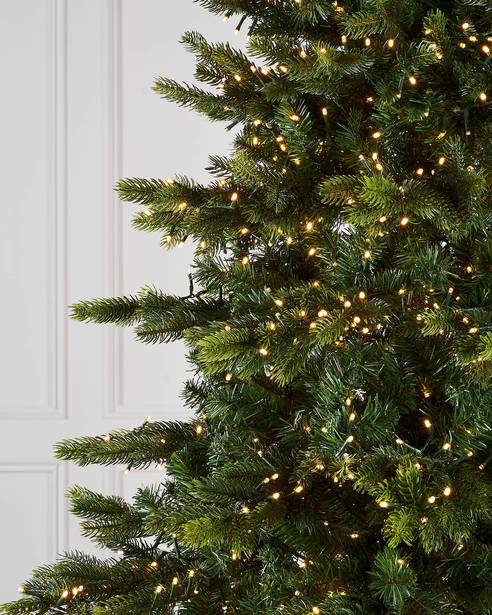 Close-up of a Christmas tree with lights against a white door background.