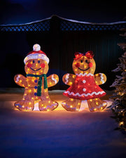 LED gingerbread man and gingerbread lady on snowy grass on a dark background