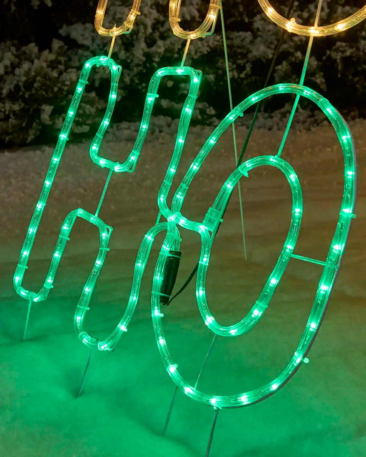 LED lighted decorative sign spelling 'Ho' in bright green, with gold lighted lettering at the top, photographed outdoors at night.