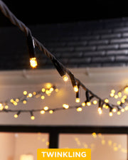 Close-up of warm white LED Christmas string lights with a focus on the twinkle or flashing feature, displayed against a blurred background of similar lights creating a cozy, festive atmosphere.