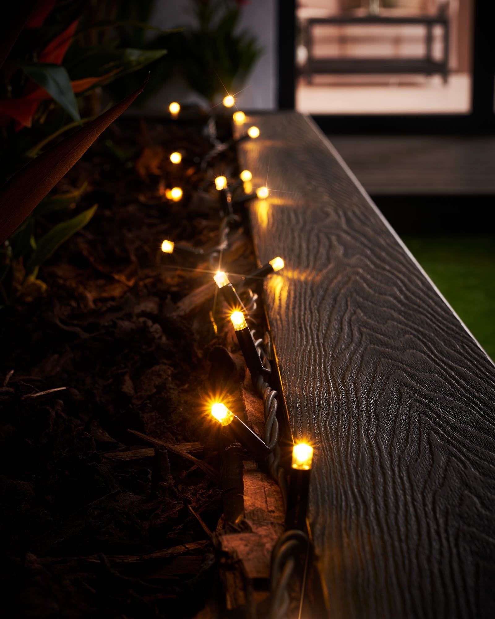 Close-up of warm white LED Christmas string lights with a focus on the twinkle or flashing feature, displayed against a blurred background of similar lights creating a cozy, festive atmosphere.